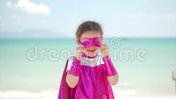 美丽的小女孩在超级英雄服装穿着粉红色斗篷和面具的英雄坐在飞机上视频的预览图