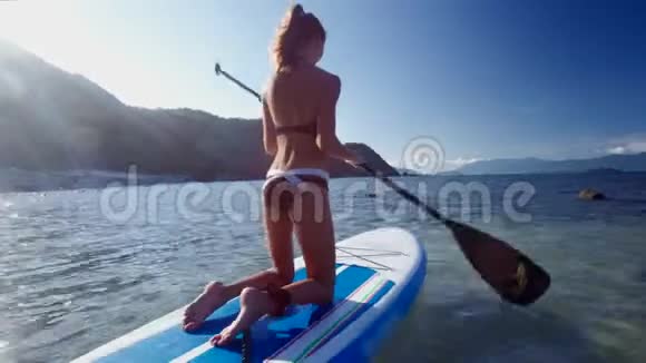 穿比基尼的金发女孩在桨板背面经过视频的预览图
