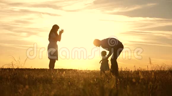 日落时分爸爸妈妈在公园里和孩子玩耍孩子迈出了第一步快乐的小女儿和妈妈玩视频的预览图