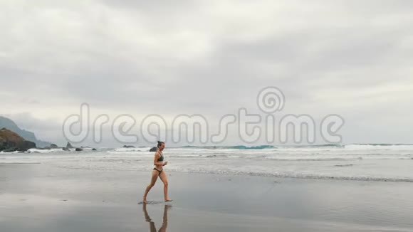 在加那利群岛的特内里费在暴风雨中的贝尼霍海滩上慢跑的迷人年轻女子的追踪镜头女选手视频的预览图