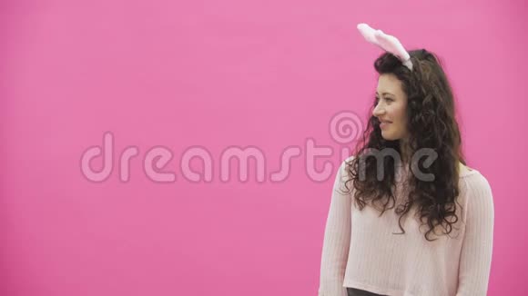 粉红色背景的年轻创意夫妇头上戴着黑黑的耳朵在这段时间里这个人给了一个带兔子的软玩具视频的预览图