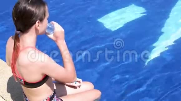 穿着泳装的可爱少女在泳池边喝水健康的生活方式暑假视频视频的预览图