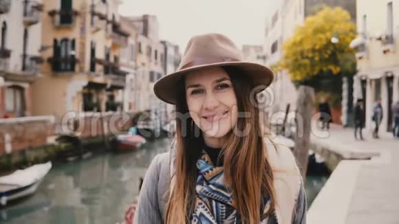 意大利著名的威尼斯运河旁戴着帽子微笑的年轻美丽的欧洲女游客的特写肖像视频的预览图