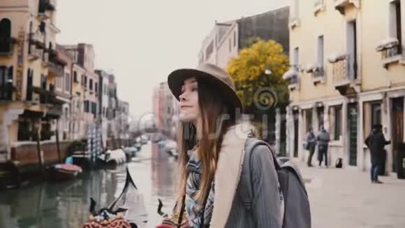 快乐年轻时尚的欧洲女游客戴着帽子在意大利著名的威尼斯运河旁四处张望视频的预览图