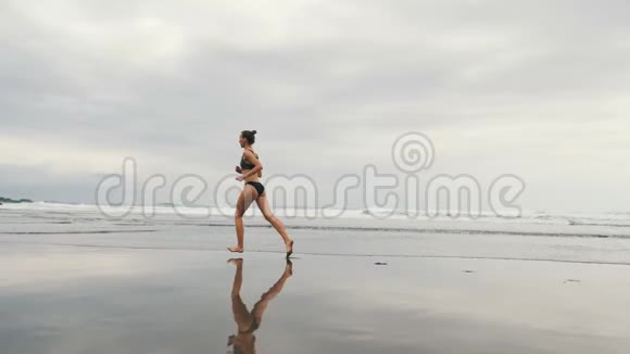 在加那利群岛的特内里费在暴风雨中的贝尼霍海滩上慢跑的迷人年轻女子的追踪镜头女选手视频的预览图