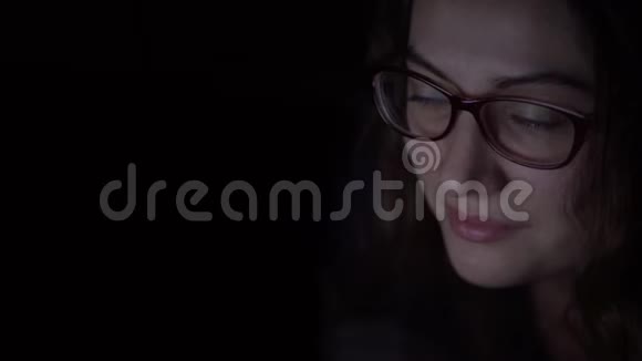 戴眼镜的女孩晚上用笔记本电脑躺在床上孤立光视频的预览图