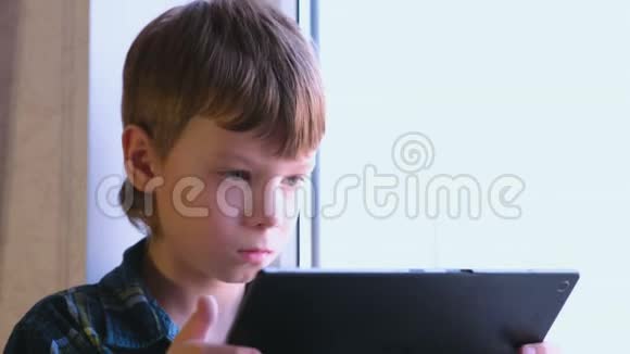 活泼的男孩坐在窗台上看书坐在平板电脑里视频的预览图