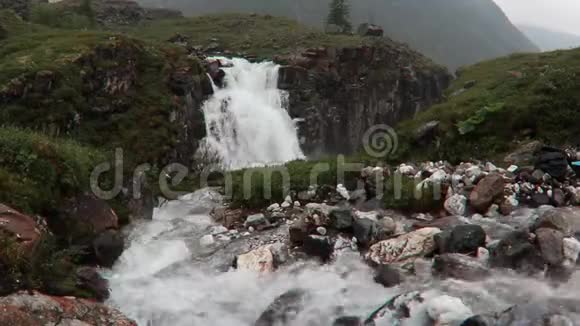 瀑布流淌在岩石和绿草的山脉中冰岛朦胧的风景视频的预览图