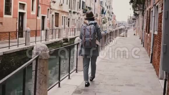 快乐年轻时尚的欧洲女游客带着相机沿着意大利威尼斯著名的老运河街道散步视频的预览图