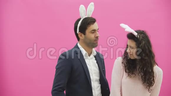 年轻夫妇站在粉红色的背景上在此期间他们进行兔子的运动女人把视频的预览图