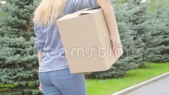 年轻女子背着一个纸板箱在户外散步视频的预览图