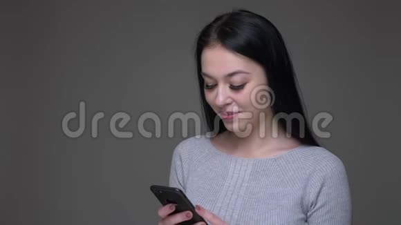 年轻漂亮的黑发白种人女性在手机上浏览社交媒体并与背景做出反应的特写镜头视频的预览图