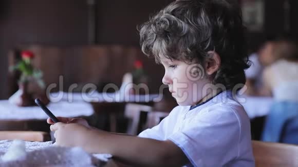 小男孩在咖啡馆拿着手机视频的预览图