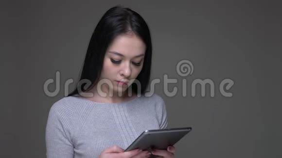 年轻漂亮的黑发白种人女性在平板电脑上浏览的特写镜头背景与灰色隔离视频的预览图
