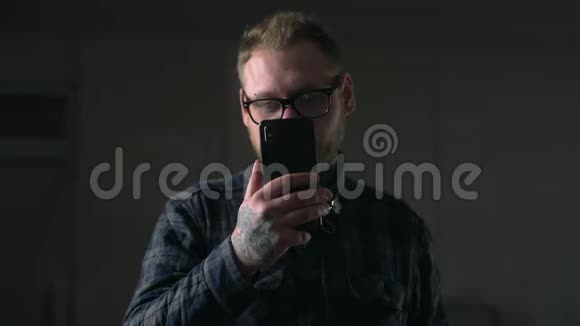 戴眼镜的人在黑暗的环境中仔细地看着他的手机拿着小玩意的人上网看着视频的预览图