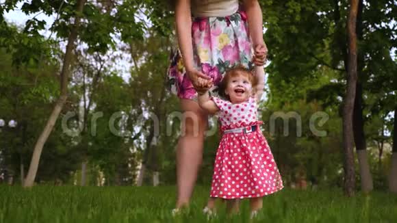宝贝在空气中旋转着妈妈的手和笑声小女儿和妈妈在公园的草地上玩耍视频的预览图