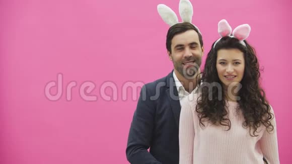粉红色背景的年轻创意夫妇头上戴着黑黑的耳朵在此期间他们展示了视频的预览图