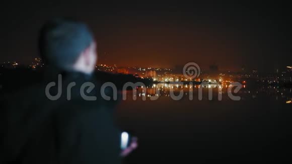 特写镜头男焦点之外在河岸边观看夜城视频的预览图