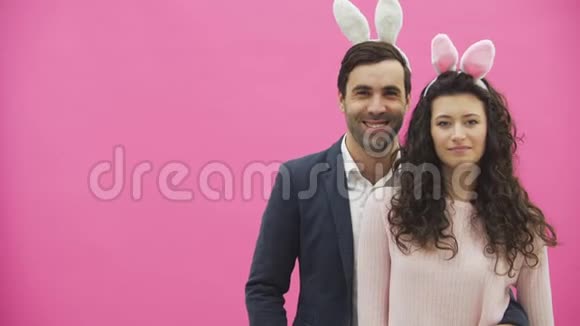 粉红色背景的年轻创意夫妇头上戴着黑黑的耳朵在这期间两个人展示了视频的预览图