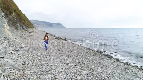 在岩石和海洋背景上做深蹲运动的女孩在呼吸练习时猛击身体视频的预览图