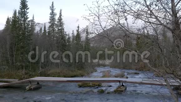 一个男子旅行者穿过一条山溪越过一座桥美丽的景色他在智能手机上拍摄风景视频的预览图