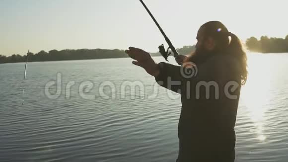 长胡子的人拿着钓鱼竿站在河岸上钓鱼渔夫把鱼竿扔进河里河流视频的预览图