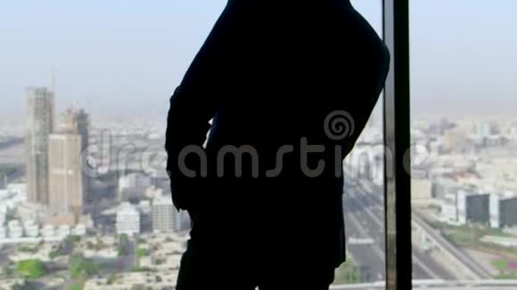 一个穿西装的商人手拿着智能手机站在窗外的后视镜里库存公司视频的预览图