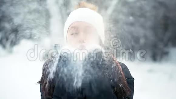 一个戴着白色帽子的年轻女孩在镜头上吹着一把雪视频的预览图