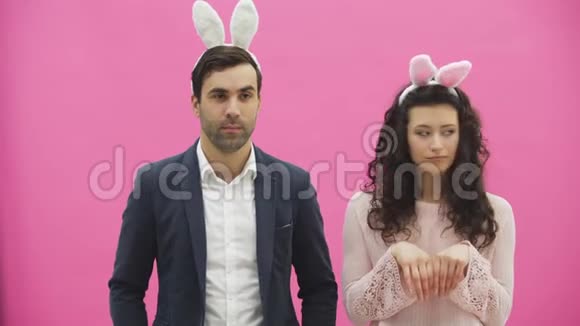 年轻漂亮的夫妇站在粉红色的背景上在这期间他们穿着杂乱的耳朵温柔地看着视频的预览图