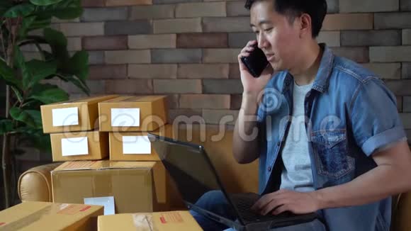 亚洲男性企业家在家中使用笔记本电脑和带盒的电话视频的预览图