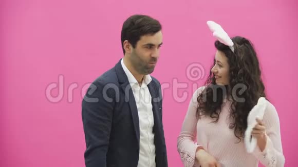 年轻情侣的粉色背景头上戴着黑黑的耳朵在这期间女孩戴着兔子耳朵视频的预览图