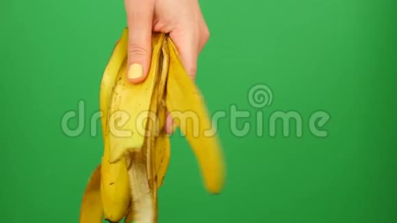 带有黄色指甲的女性手将香蕉皮放在绿色背景铬键上视频的预览图