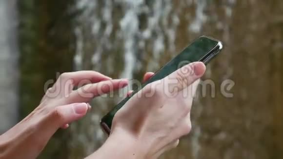 女人在大自然中使用智能手机的背景是瀑布依赖互联网生态旅游概念视频的预览图
