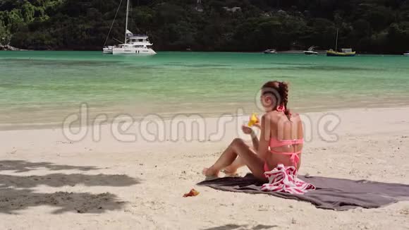 一个美丽的年轻女孩坐在海滩上用防晒霜涂抹她的身体视频的预览图