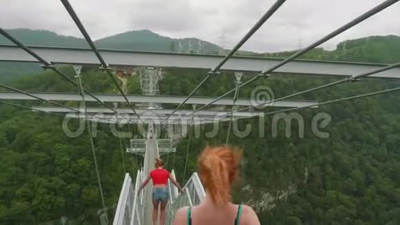 镜头跟随白种人年轻的运动女子滑稽地走在高高的高山上悬挂着的特里利斯桥上视频的预览图