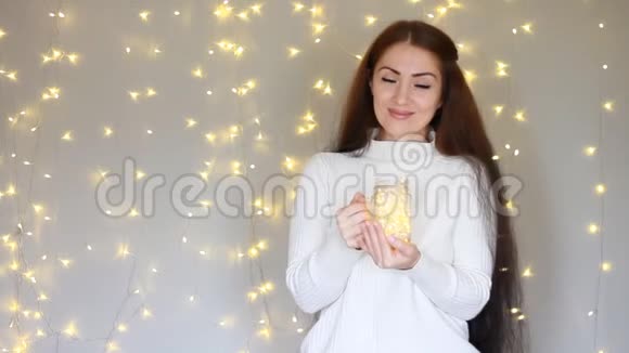 美丽的女人穿着白色毛衣微笑着手里拿着一盏灯在灯光的背景下做梦视频的预览图