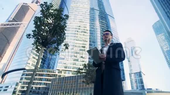 男经理正在沿着由摩天大楼组成的商业综合体散步6K电影院的镜头视频的预览图