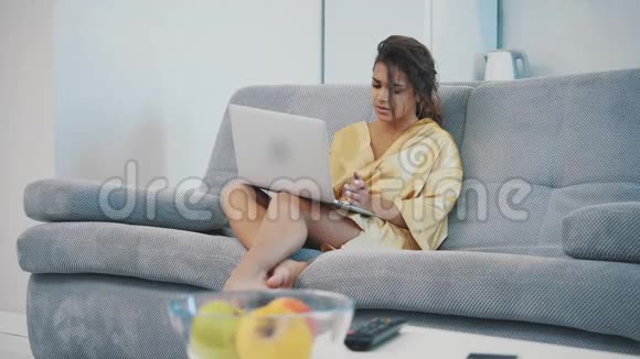 穿着睡衣坐在沙发床上的年轻女子使用笔记本电脑很紧张家庭氛围视频的预览图