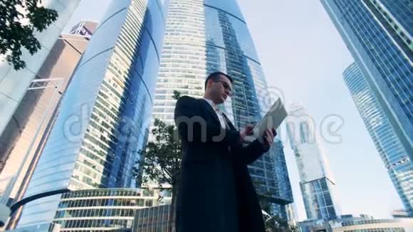 成功的商人正站在摩天大楼旁边操作他的平板电脑6K电影院的镜头视频的预览图
