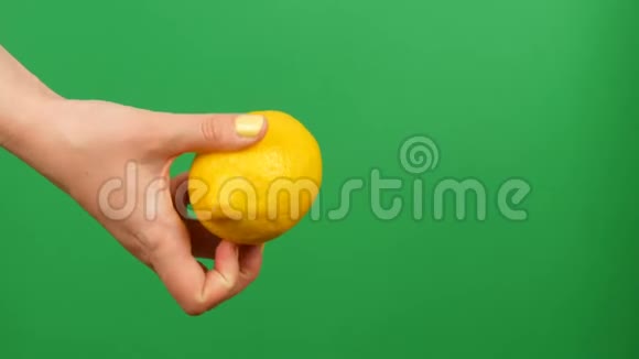 带有黄色指甲的女性手在绿色的关键背景上拿着柠檬视频的预览图