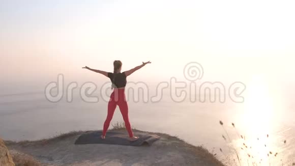 美丽的景色女人做瑜伽伸展在山上日落时的海景伸展手臂视频的预览图