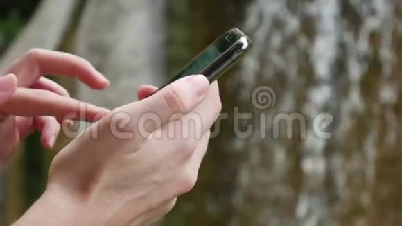 女人在大自然中使用智能手机的背景是瀑布依赖互联网生态旅游概念视频的预览图