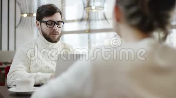 成年男子在咖啡馆的一张桌子旁用笔记本电脑与女友交谈视频的预览图