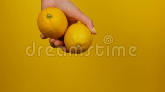 黄色指甲的女性手拿着两个黄色背景的柠檬视频的预览图