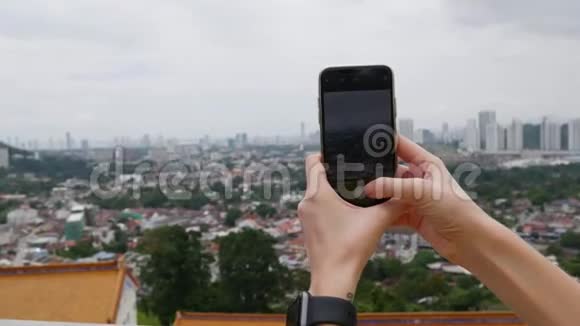 年轻女子在站在山上的智能手机上制作城市的垂直照片镜头越过肩膀多云视频的预览图