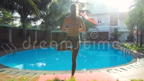 后景女孩早上站在游泳池旁做瑜伽姿势视频的预览图