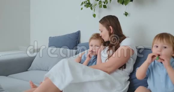 妈妈抱着两个小儿子在客厅的沙发上看电视家庭看电视视频的预览图