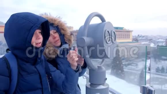在冬天妈妈和儿子通过望远镜在城市的屋顶上看视频的预览图