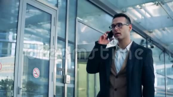 男专家正沿着一栋办公楼的玻璃墙走着在打电话6K电影院的镜头视频的预览图