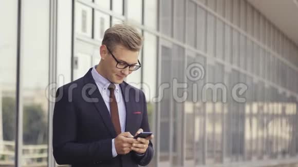 快乐的商人微笑着看着站在办公室外面的短信时尚的男性执行经理视频的预览图